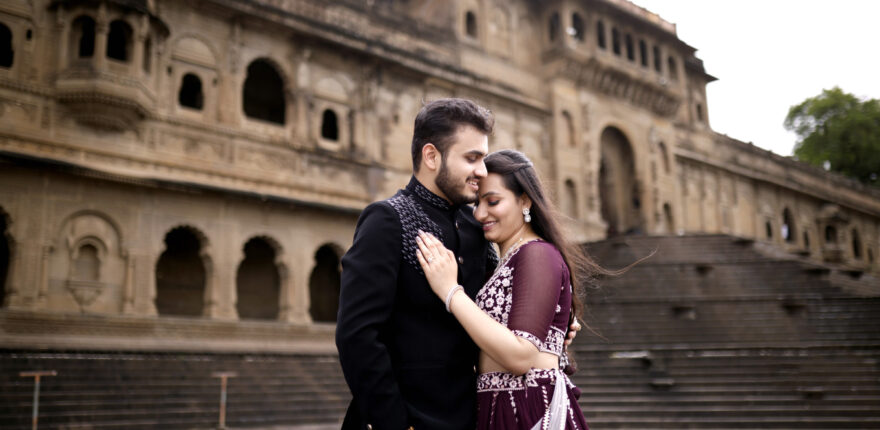 A dreamy pre-wedding moment captured in the heart of Indore — a couple embraces in a scenic location surrounded by natural beauty and timeless architecture. The bride-to-be glows in a flowing pastel gown while the groom stands dashing beside her in a tailored suit. The soft golden hour light adds a romantic glow to the scene, making it a picture-perfect memory. Captured by Shadowgraphy Studio, a top-rated pre wedding photographer in Indore, this image blends emotion with elegance.