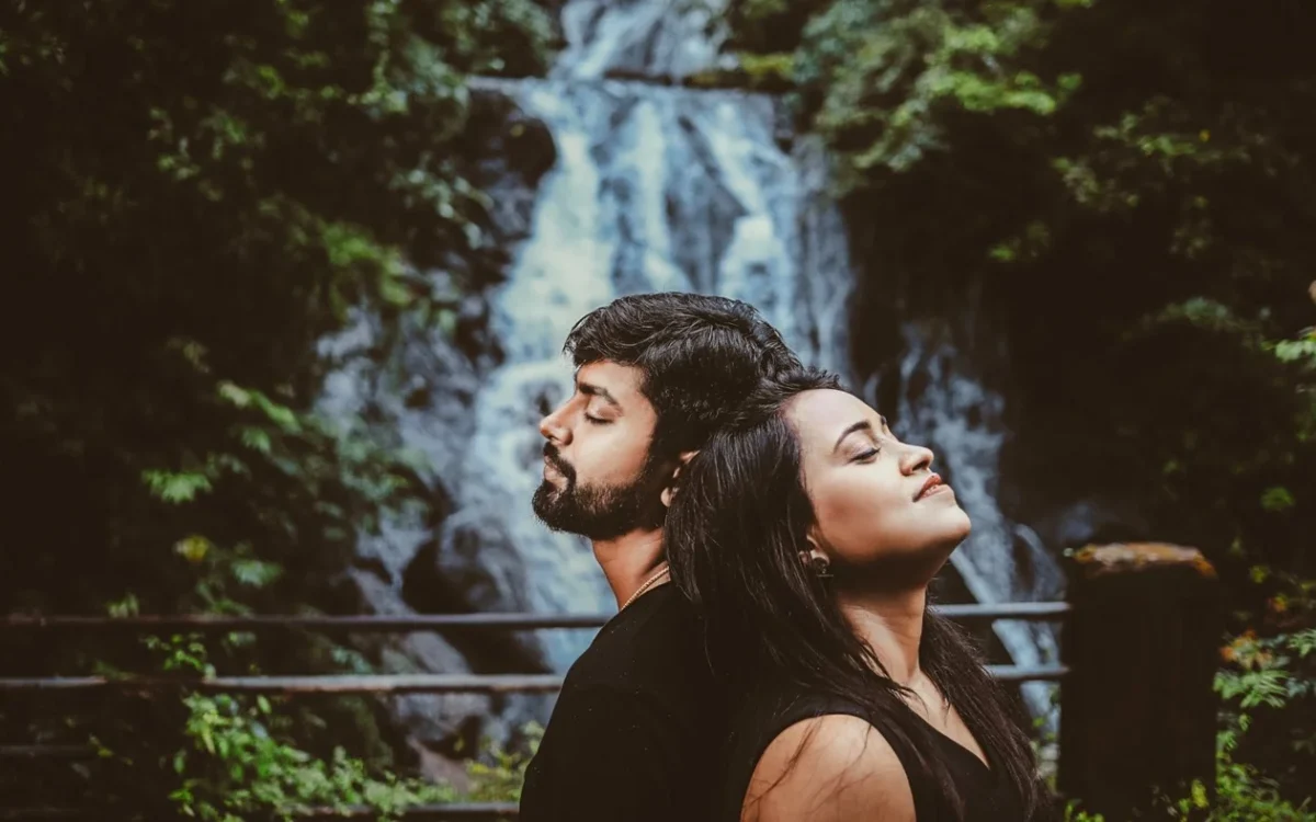 Indian couple standing close with eyes closed in front of a forest waterfall during a soft-light pre-wedding shoot near Indore