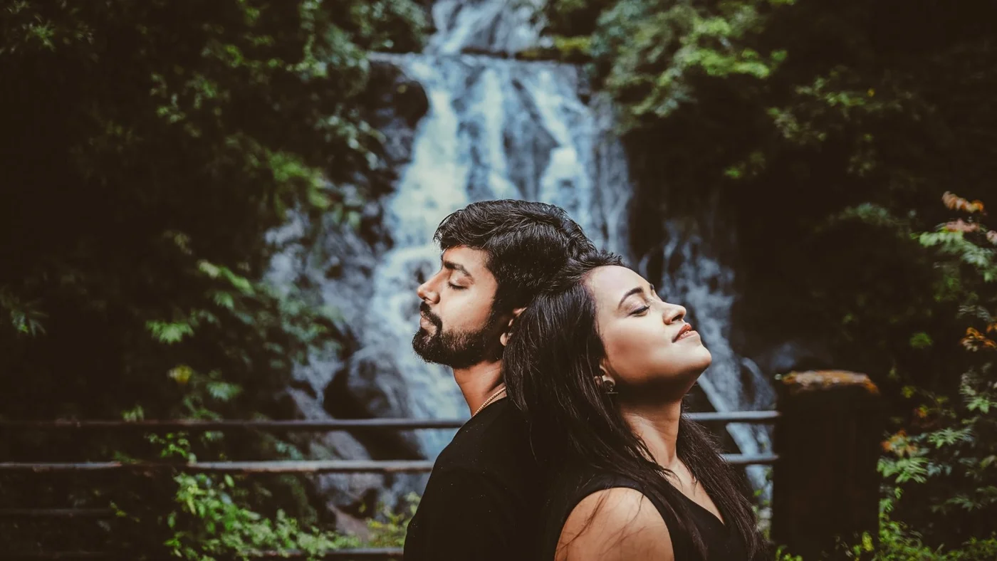Indian couple standing close with eyes closed in front of a forest waterfall during a soft-light pre-wedding shoot near Indore