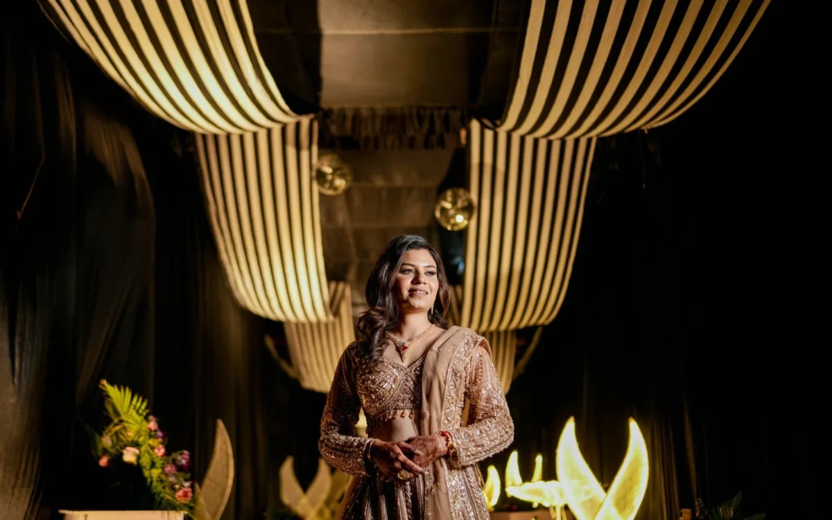 Bride in a shimmering traditional outfit standing beneath warm hanging ceiling lights