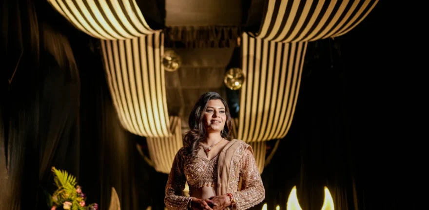 Bride in a shimmering traditional outfit standing beneath warm hanging ceiling lights