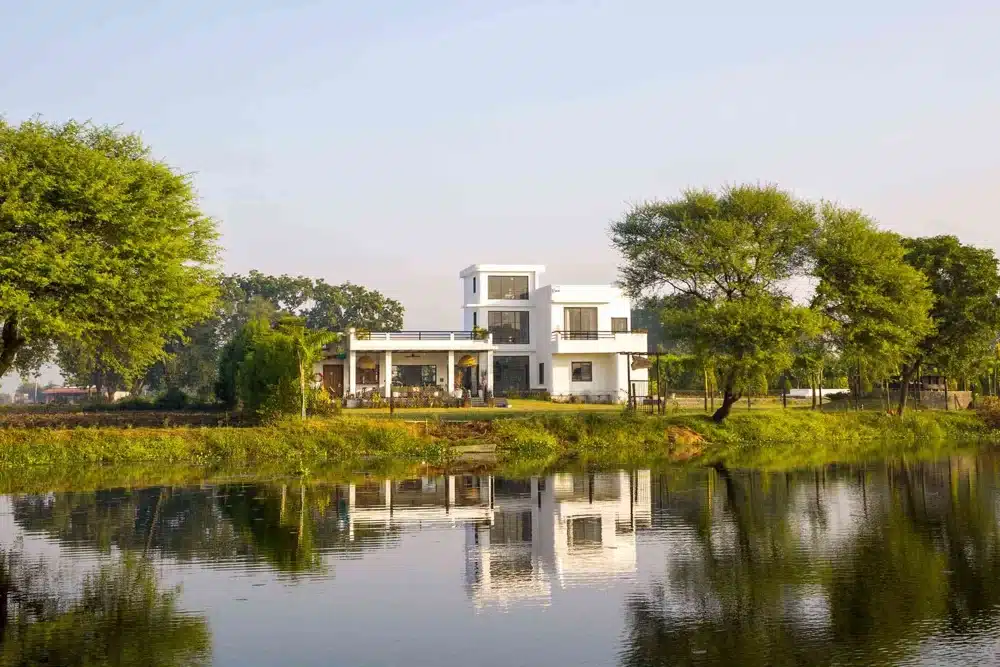 A white villa style building with green lawns and a pond in front