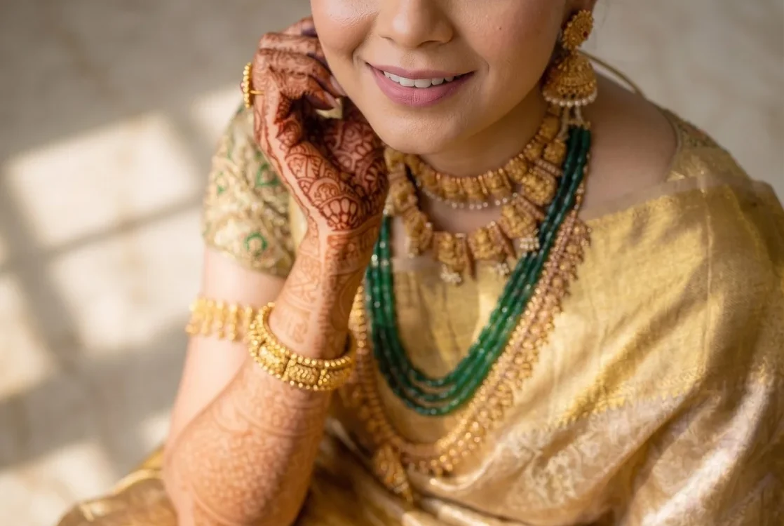 Bride in a gold saree with mehendi-decorated hands and traditional jewellery smiling naturally at her wedding, candid wedding photography in Indore