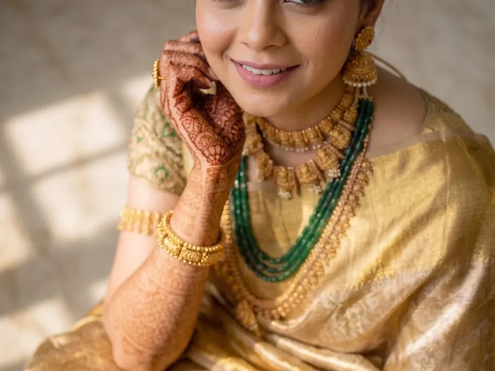 Bride in a gold sari and green jewellery looking towards the camera in a seated portrait