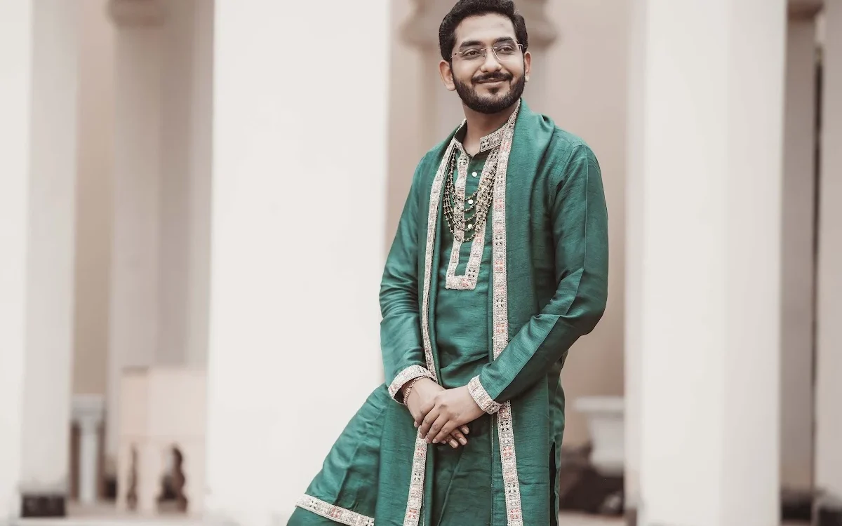 Groom in a teal sherwani with dupatta and mojari shoes standing on marble steps