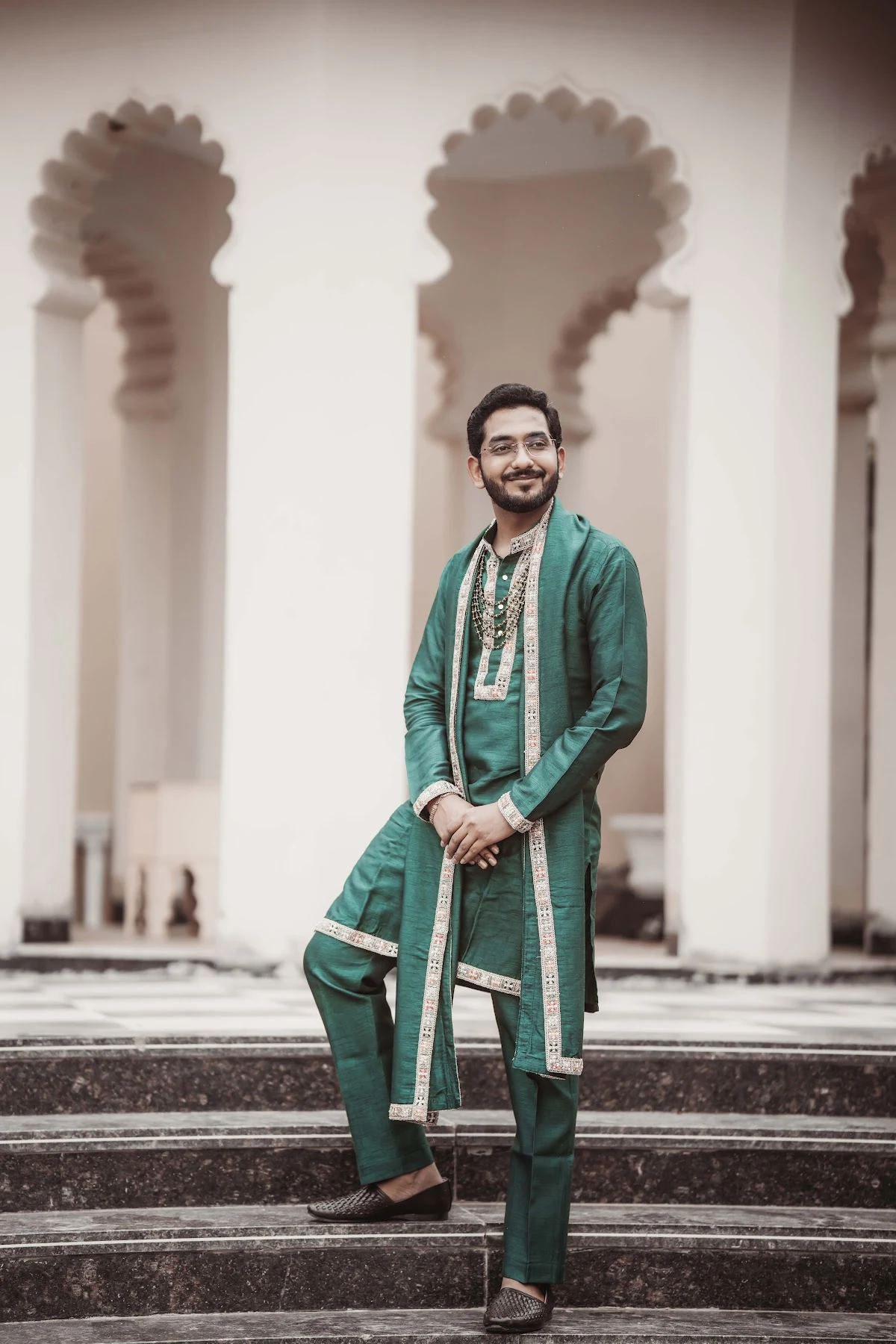 Groom in a teal sherwani with dupatta and mojari shoes standing on marble steps
