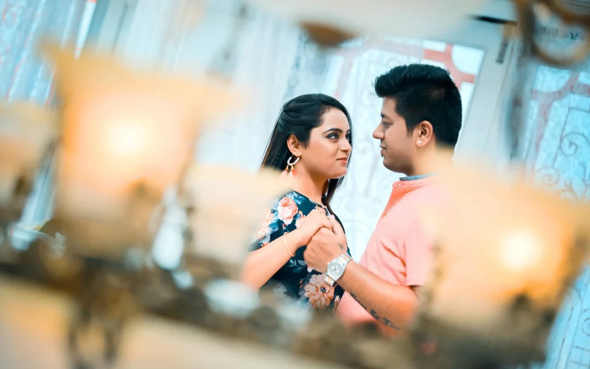Couple holding hands and facing each other, framed through warm decorative wedding lights