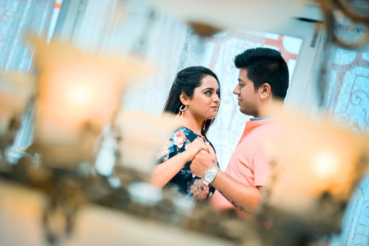 Couple holding hands and facing each other, framed through warm decorative wedding lights