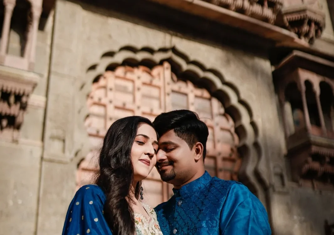 Couple in coordinated blue traditional outfits sharing a quiet moment beneath an ornate carved stone arch