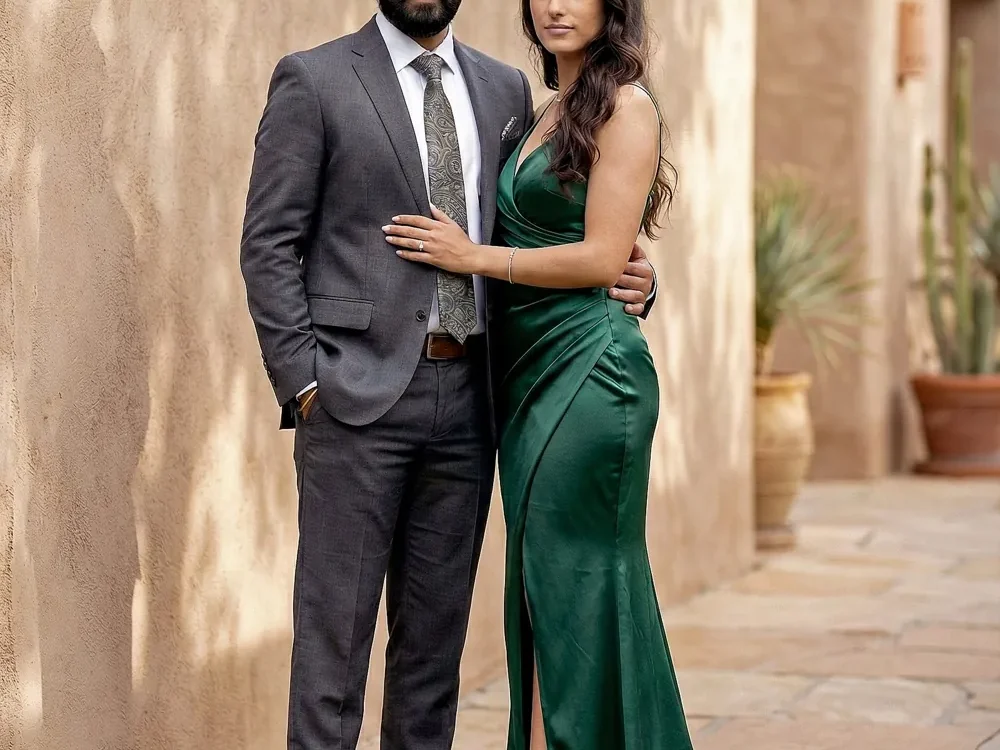 Couple in a grey suit and green gown standing beside a textured wall in an outdoor portrait