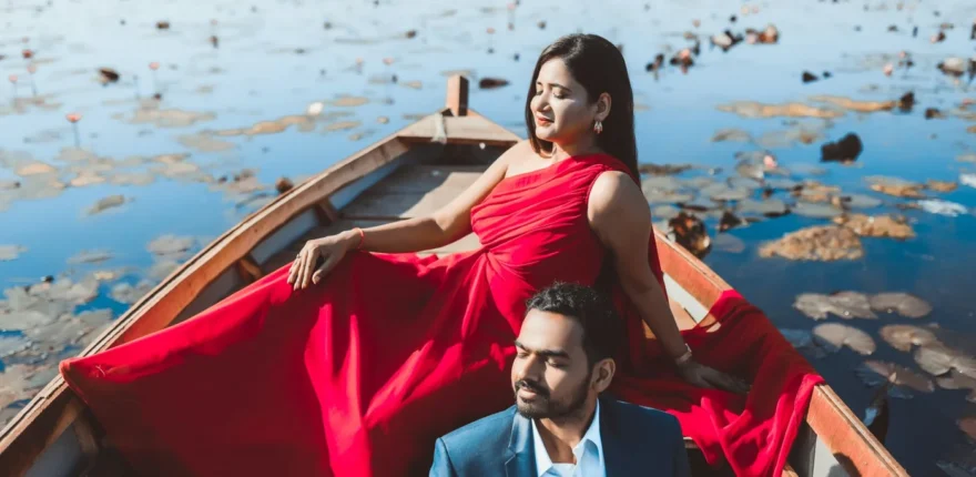 Couple in a wooden boat on a lily pond, woman in a flowing red gown and man in a navy blazer, relaxed pre-wedding shoot near Indore