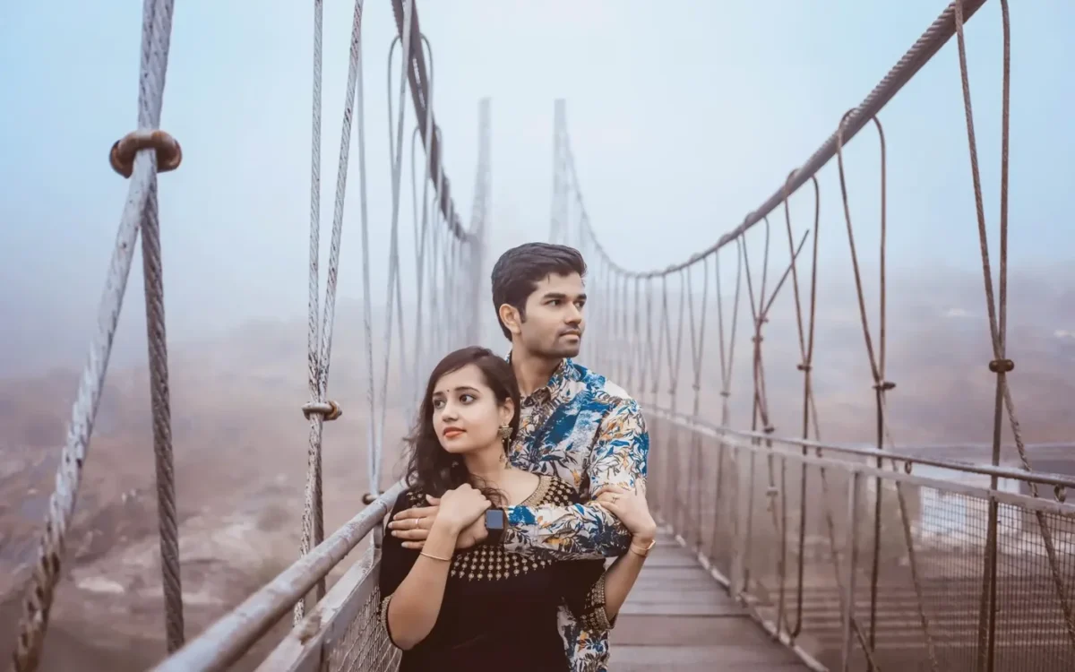 Couple embracing on a misty suspension bridge, the man in a floral shirt with his arms around the woman