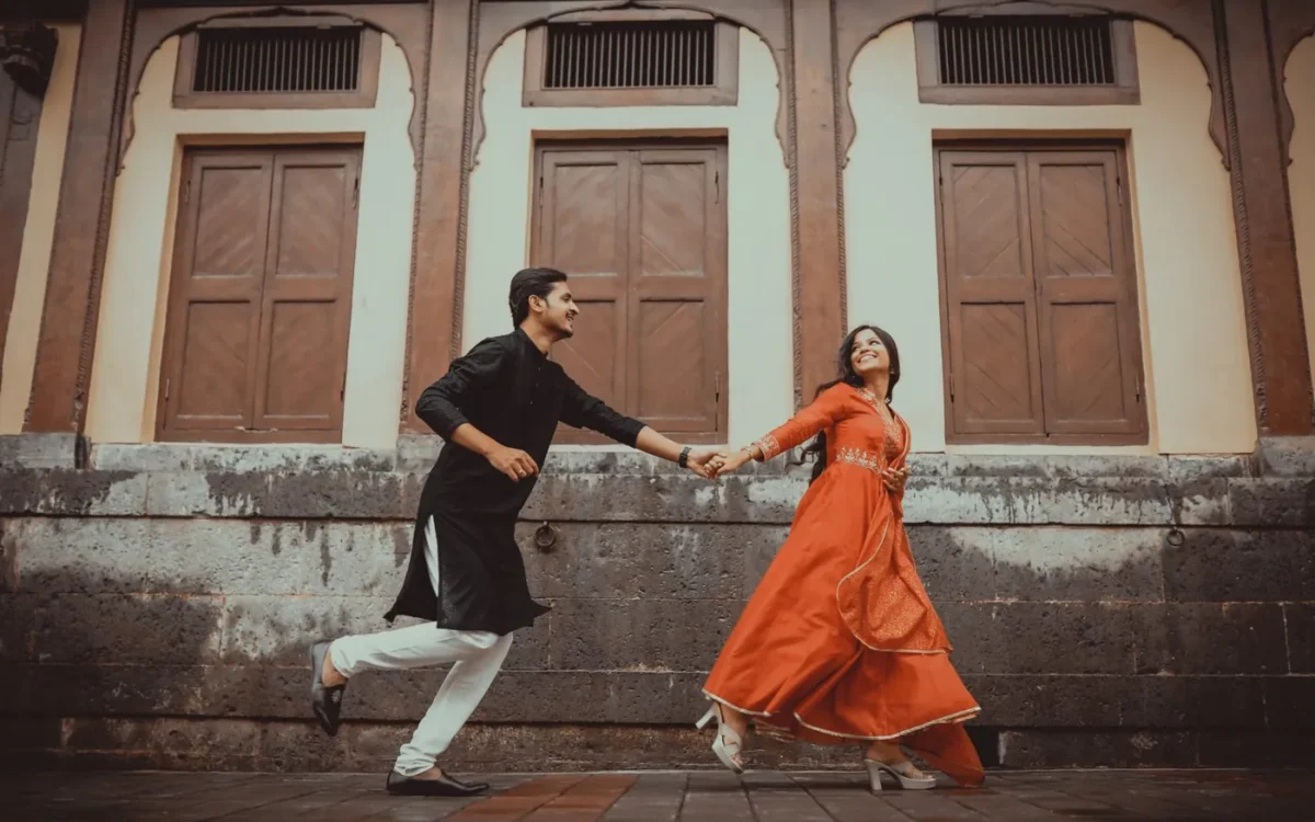 Couple holding hands in black and orange traditional outfits during a moving outdoor portrait