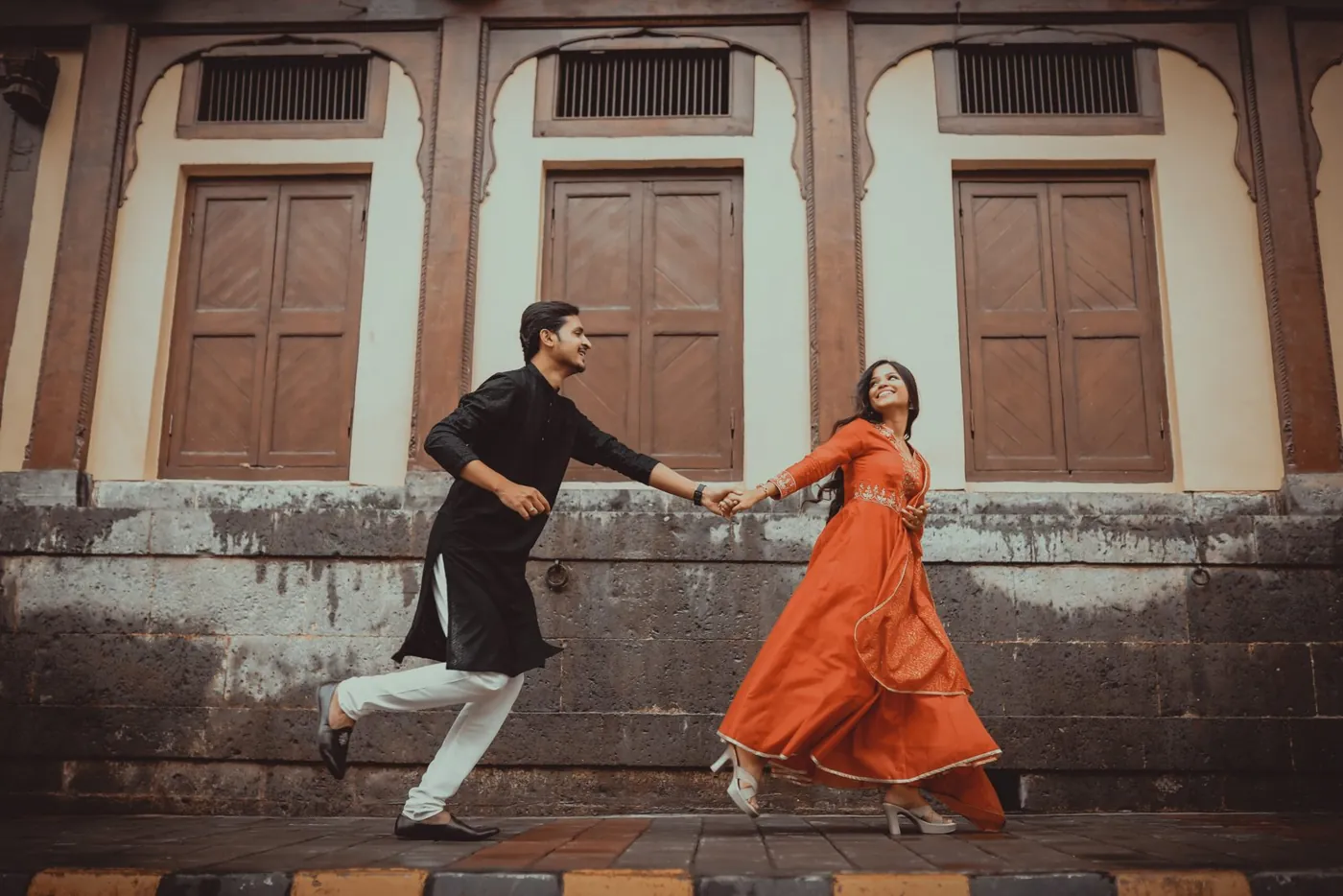 Couple holding hands in black and orange traditional outfits during a moving outdoor portrait