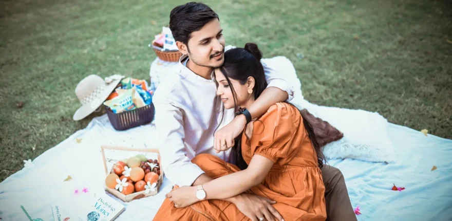 Romantic pre wedding shoot ideas picnic couple Indian couple sitting close on a picnic blanket on a lawn with fruit and a hat, a romantic pre-wedding shoot idea near Indore