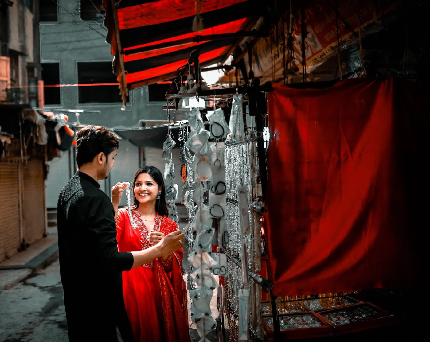 Couple in black and red outfits smiling beside a jewellery stall beneath a red awning