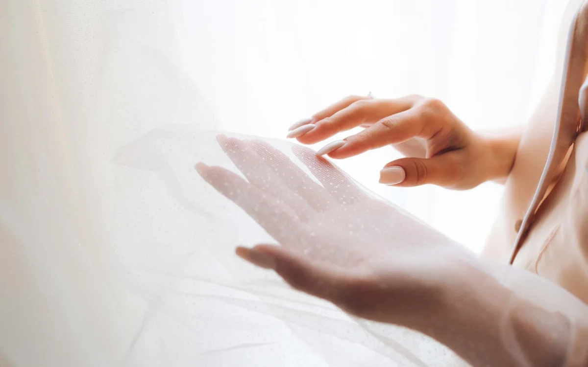 Hands gently holding a soft white wedding veil