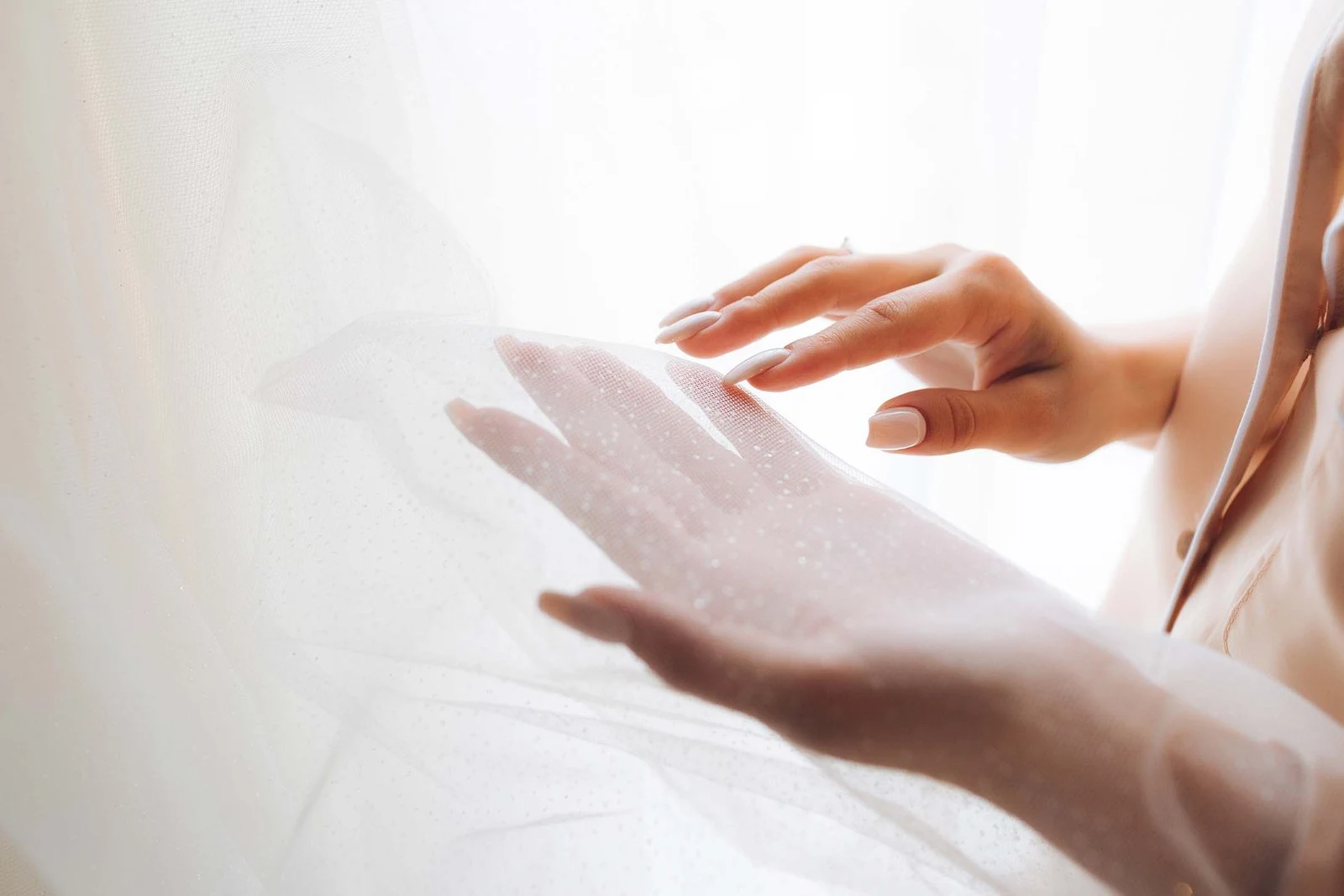 Hands gently holding a soft white wedding veil