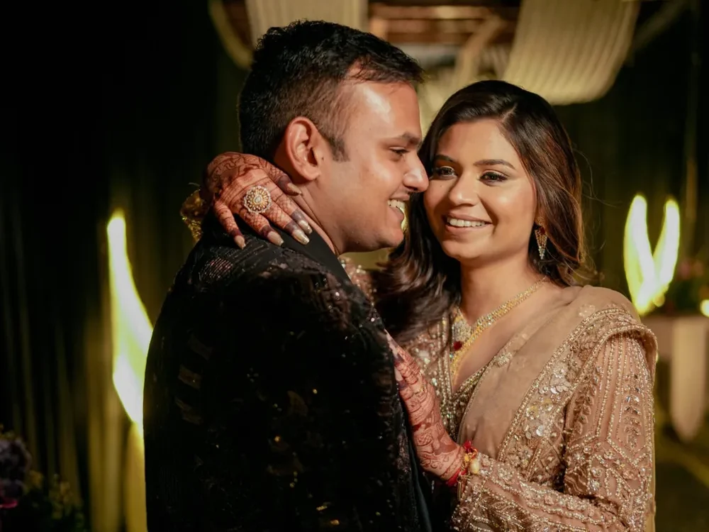 Couple in embellished evening outfits embracing beneath warm indoor lights