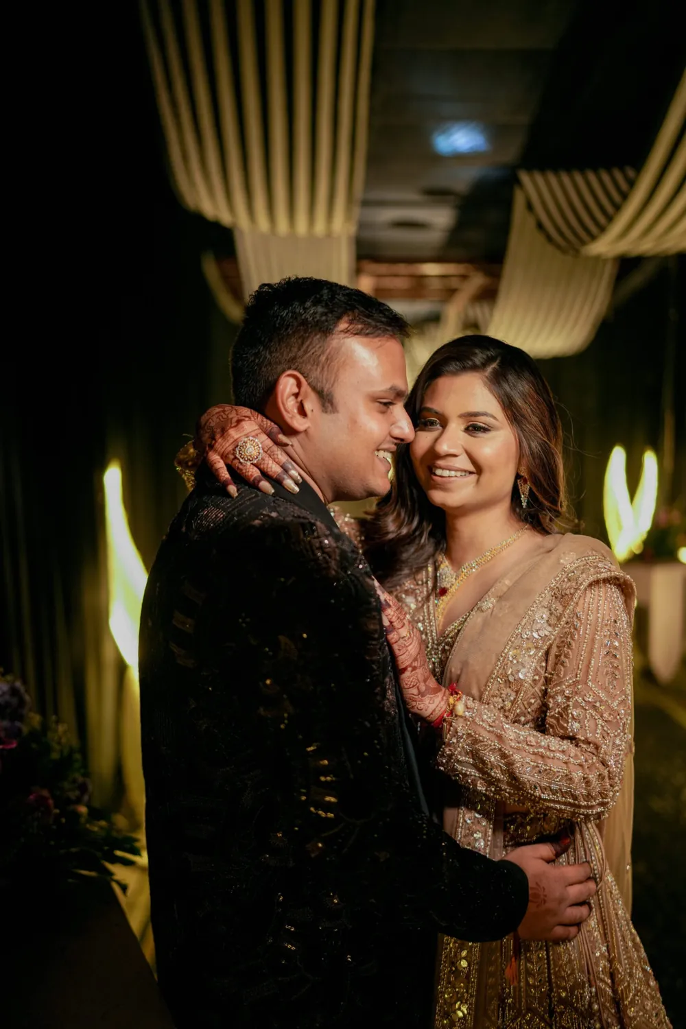 Couple in embellished evening outfits embracing beneath warm indoor lights