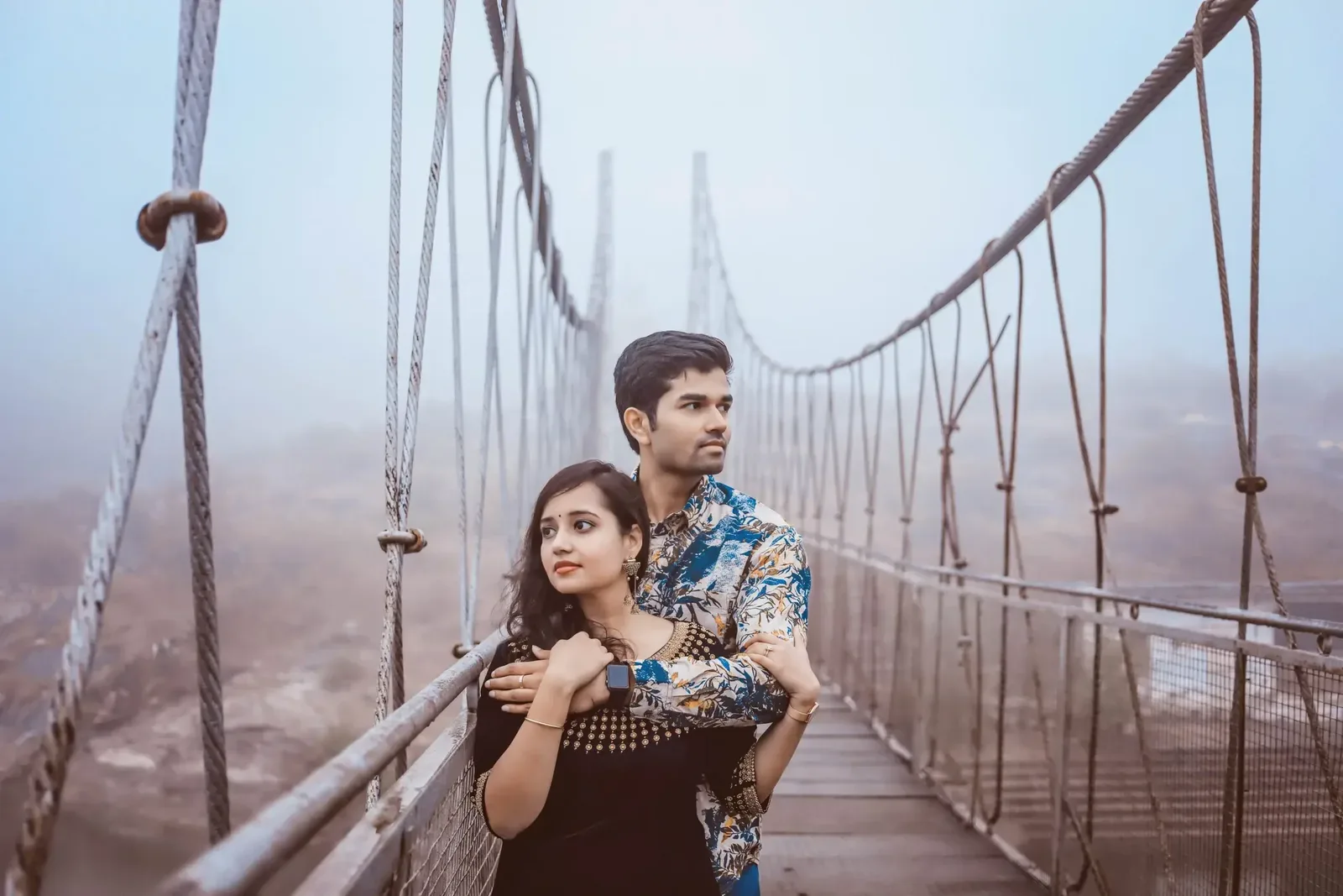 Couple embracing on a misty suspension bridge during an outdoor portrait session
