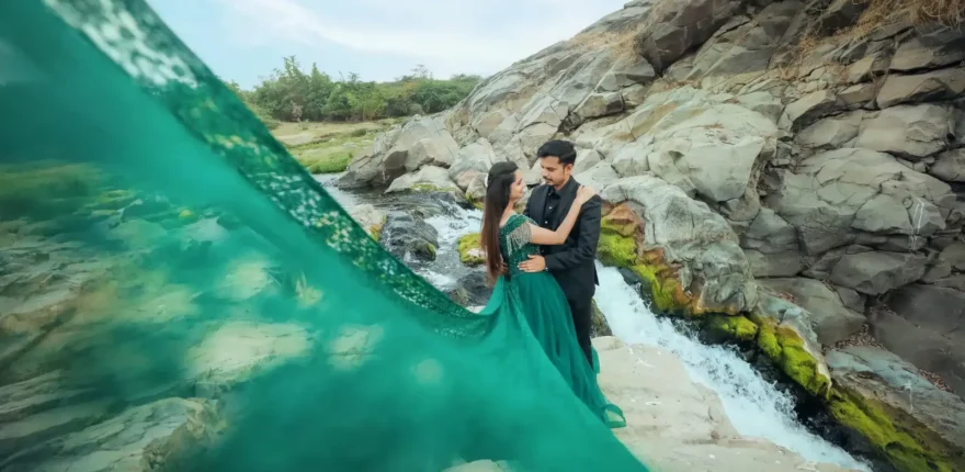 Couple standing by a waterfall with a long flowing green gown, pre-wedding shoot
