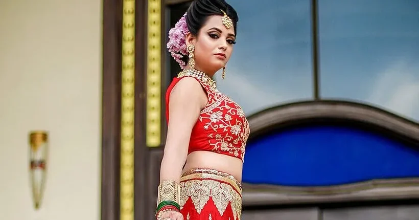 Bride in red lehenga with flowers in her hair posing by a window