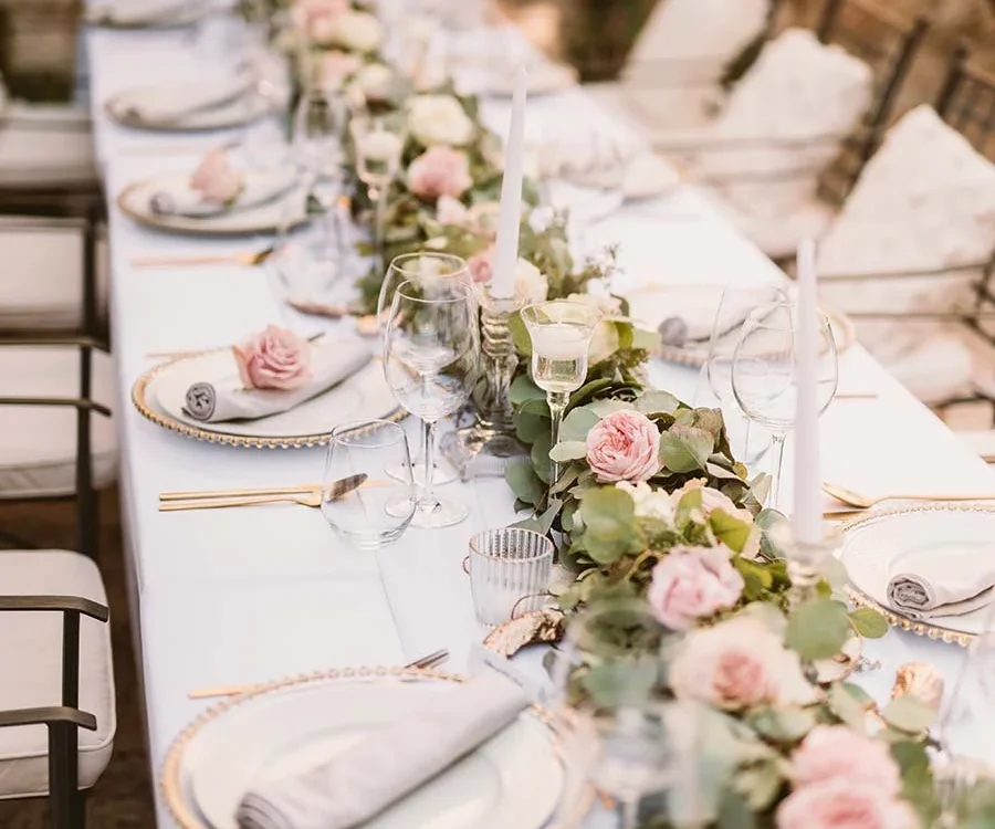 Long wedding reception table set with white linens, pink roses and gold rimmed plates