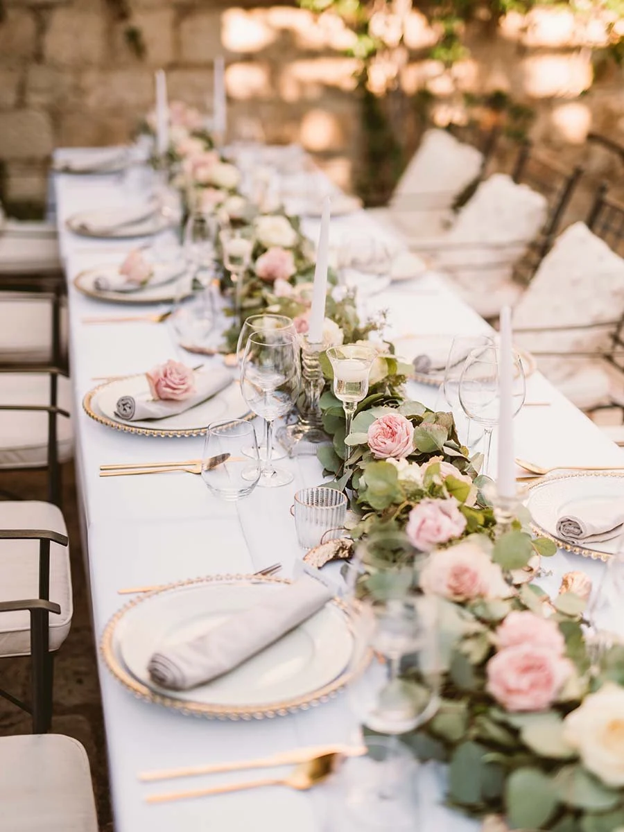 Long wedding reception table set with white linens, pink roses and gold rimmed plates